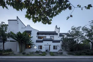 A large Asian-style house with white walls, green roof tiles, and multiple rooms, featuring a living area and dining area, with several windows providing natural light