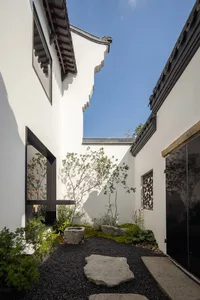 A serene courtyard with a white building, plants, rocks, and decorative vases, creating a peaceful atmosphere