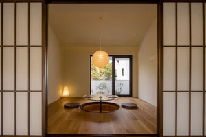 A cozy living area with a wooden floor, a round table, and three chairs, featuring a potted plant and a vase for decoration
