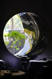 Elegant dining space with a round table, chairs, potted plants, and a clock on the wall, set in a restaurant-like atmosphere