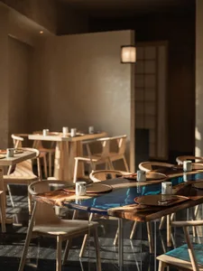 A restaurant dining area with wooden tables and chairs, set with plates and bowls, creating an inviting atmosphere