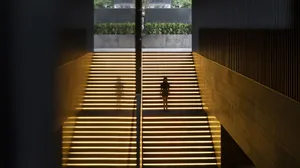 A well-lit hotel staircase with a wooden staircase featuring yellow stripes, two people walking up the stairs