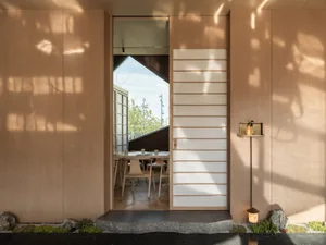 燈光柔和的用餐區，配有大型木桌與椅、木質牆板，以及通往建築物其他區域的門口