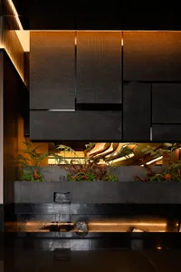 A modern bathroom with a black countertop featuring a waterfall fountain, surrounded by potted plants, creating a relaxing atmosphere