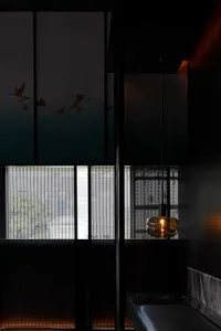 A dark interior space with a black wall and a window, featuring two birds flying in front of the window