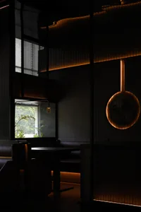 A cozy restaurant dining area with black walls, natural light, and a large table surrounded by chairs