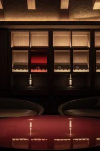 Darkly lit room with two chairs and a red table, surrounded by bottles of liquor