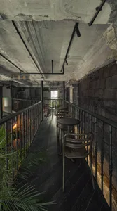 A modern cafe with a balcony overlooking another area, featuring chairs, dining tables, potted plants, and a comfortable atmosphere