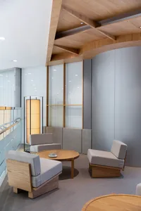 Modern living space with a large window, a couch, a chair, and a dining table, well lit and empty except for two cups on surfaces