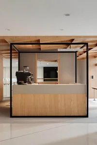 Warm and inviting coffee shop interior with wooden walls and floors, natural light from a large window, and two cafes