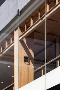 A modern building with a glass wall and wooden panels on its facade, showcasing the contrast between the two materials and the natural light entering through the glass wall