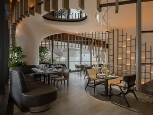 Warm and inviting restaurant interior with wooden floors and walls, featuring dining tables, chairs, potted plants, and wine glasses