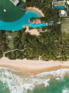 Aerial view of a beachfront property with a house, pool, and people enjoying the beach atmosphere
