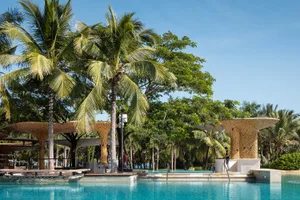 A leisurely outdoor pool area surrounded by palm trees, with people relaxing on poolside chairs and taking in the view