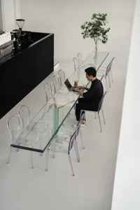 Casual dining space with a glass table, chairs, and people using a laptop and sitting nearby