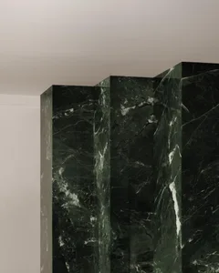 A large indoor space with a green marble wall featuring three distinct sections with different textures and patterns, exuding sophistication and refinement