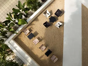 A casual outdoor seating area with black lounge chairs and potted plants on a sandy ground, conveying a relaxed atmosphere