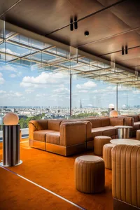 A modern living area with large windows, brown leather chairs, and multiple tables, creating a bright and open atmosphere