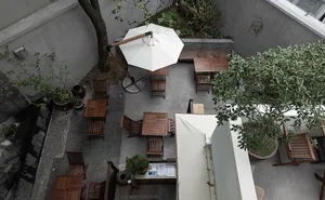 Outdoor dining area with multiple tables and chairs under a large umbrella, surrounded by a relaxed and inviting atmosphere