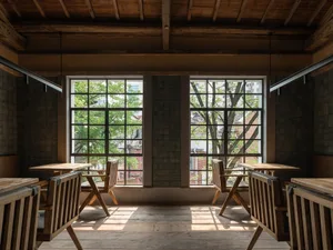 Open living area with wooden floors and walls, two dining tables, chairs, and natural light from multiple windows
