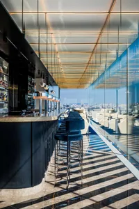 Modern bar area with a wooden counter, stools, and chairs, featuring bottles and a stylish atmosphere