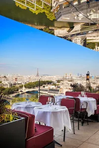 Aerial view of a Parisian restaurant with a large dining area, tables, chairs, wine glasses, and a visible kitchen, set in an elegant and inviting atmosphere