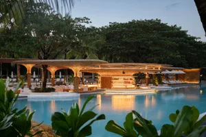 A resort pool area at night surrounded by palm trees, with chairs and umbrellas for relaxation and socializing