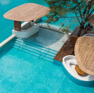 A relaxing poolside area with four patio chairs and two umbrellas providing shade around a swimming pool