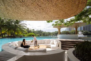 Indoor pool area with a wooden table, white couches, and a relaxed atmosphere, featuring a combination of wood and white elements