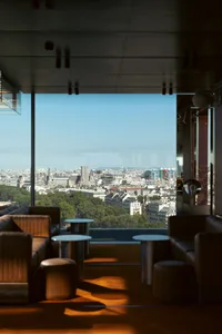 A restaurant on the top floor of a building with a glass wall offering a panoramic city view, comfortable seating, and high-end design elements