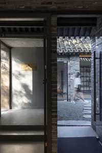 A traditional Asian building with open doors, a brick wall, and a tile roof, featuring a calm and serene atmosphere