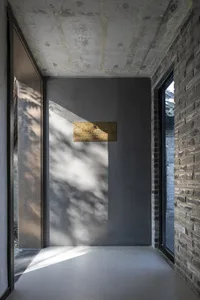 A building with a gray concrete wall and two windows, with a doorway leading to a darker area