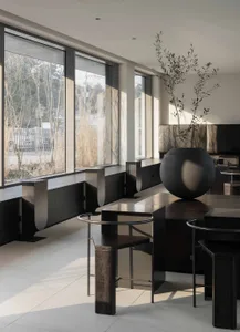 A modern restaurant with tables, chairs, and vases, lit by natural light from a large window