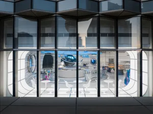 A modern dining space with a circular table surrounded by chairs, set against a sleek backdrop through a glass door
