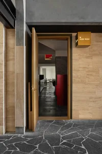 Modern restaurant interior with black flooring and walls, wooden doors, chairs, and a clock on the wall