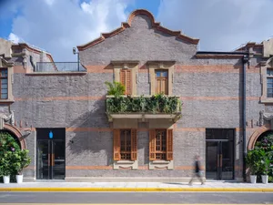 A rustic brick building with a balcony and large windows, blending traditional and modern architectural elements