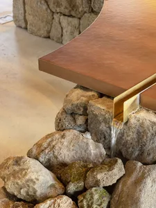 A stone table with a gold trimmed edge and a water feature, surrounded by rocks in a bright and inviting outdoor space