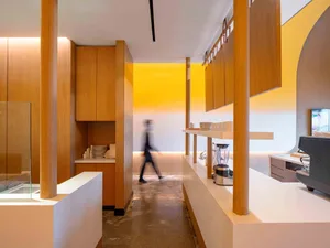 A man walks down a professional hallway with wooden walls and floors, featuring cups on surfaces and a sense of organization
