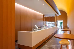 A well-lit interior design showroom with a glass display case, wooden walls, chairs, and a potted plant