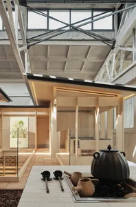 Open modern living space with wooden elements, glass surfaces, and natural light from a large window, decorated with potted plants and a vase