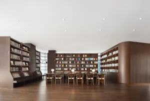 A quiet library with wooden floors and walls, featuring numerous bookshelves and chairs in a studious atmosphere