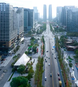 Aerial view of a city street with tall buildings, trees, cars, and pedestrians, showcasing a mix of nature and modern architecture