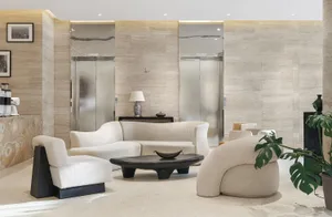 A modern living space with a white couch, carpeted floor, and several chairs, surrounded by potted plants and a vase, creating a comfortable and inviting atmosphere with clean lines and minimalist design elements