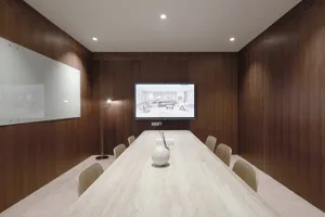 Office space with a large wooden table surrounded by chairs, a TV displaying a slideshow, and a professional atmosphere