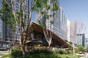 A modern restaurant building with a glass structure, surrounded by trees, and well-lit by natural sunlight