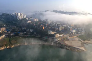 Aerial view of a city with a large body of water in front of it, surrounded by residential apartments and shrouded in fog
