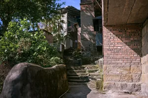 一座歷史悠久的石屋，配有磨損的石階與金屬扶手，背景似公園景觀
