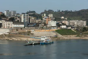 A bustling riverfront scene with a large boat and brick buildings, surrounded by people going about their daily activities