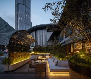 A modern restaurant patio at night with a glass structure, comfortable seating, and a cozy ambiance