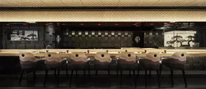 A modern bar area with a long wooden counter and unique chairs, including one resembling a rock formation, in a contemporary setting